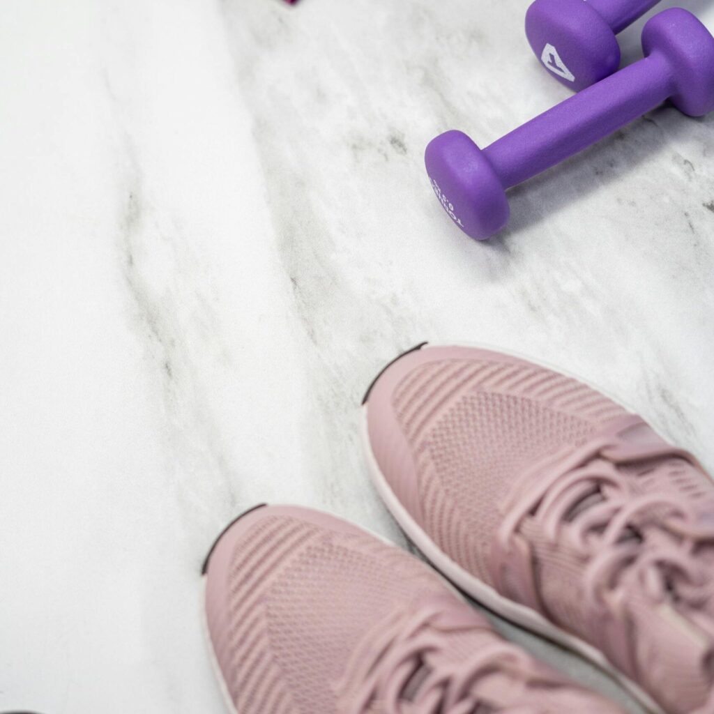 Flat lay of pastel pink fitness gear including sneakers and dumbbells on marble texture.