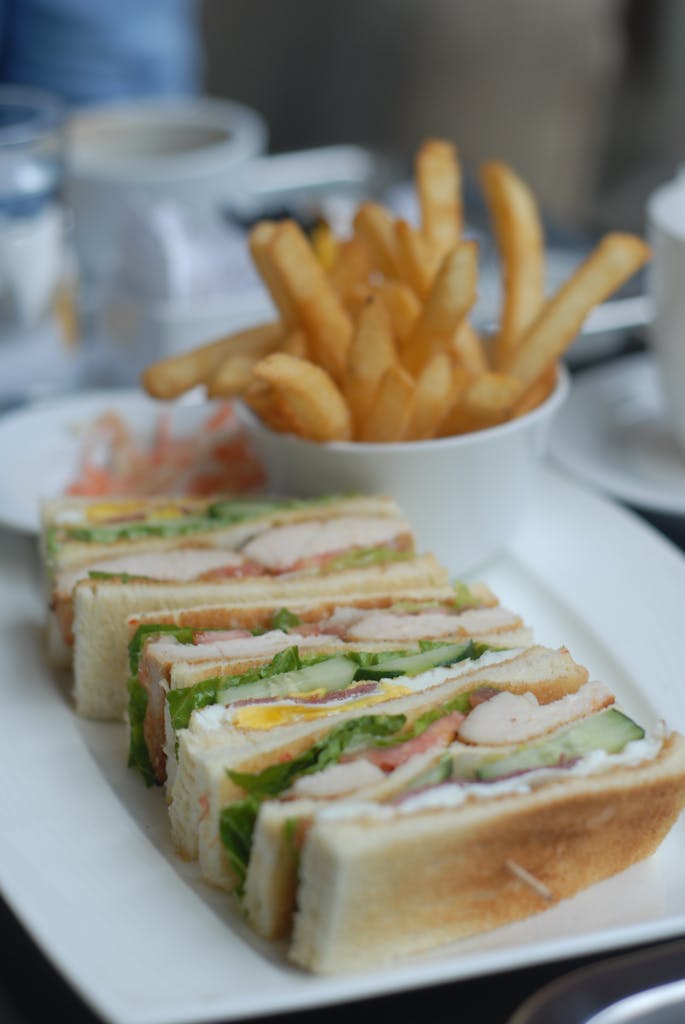 A close-up of a club sandwich paired with golden french fries on a white plate.