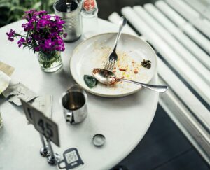 An indoor table setting with leftover food, cutlery, flowers, and a soda bottle.