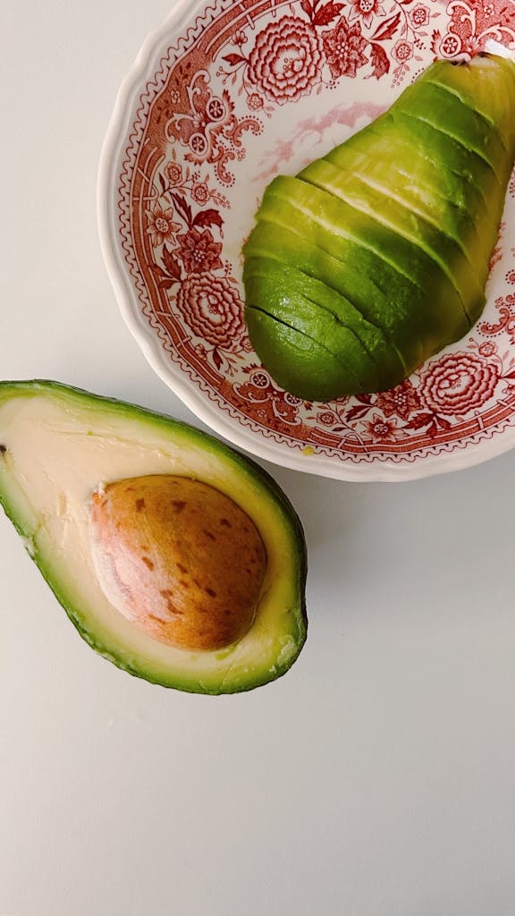 Close-up of a ripe, sliced avocado in a decorative red bowl on a white surface.