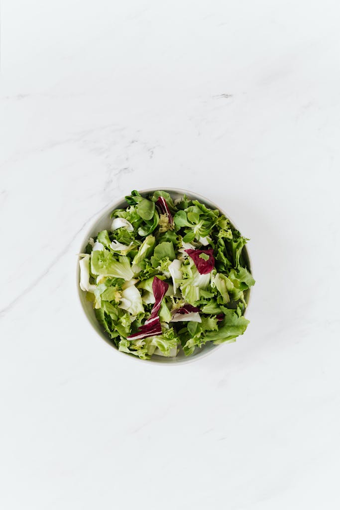 Top-down view of a fresh green salad bowl on a clean marble surface, perfect for healthy eating concepts.