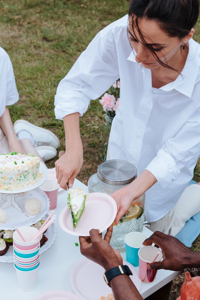 A diverse group enjoying a garden party with cake and refreshments outdoors.