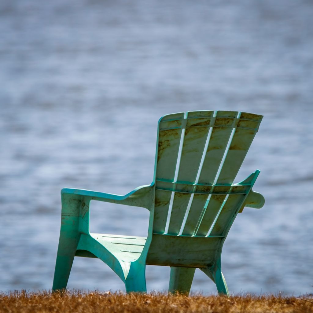 Solitary turquoise Adirondack chair facing a peaceful lakeside view.